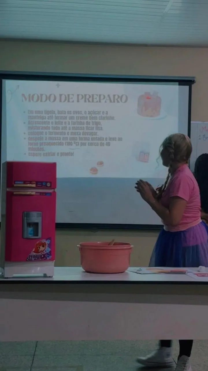Lanna Campos de rosa em uma apresentação sobre modo de preparo, diante de um telão.